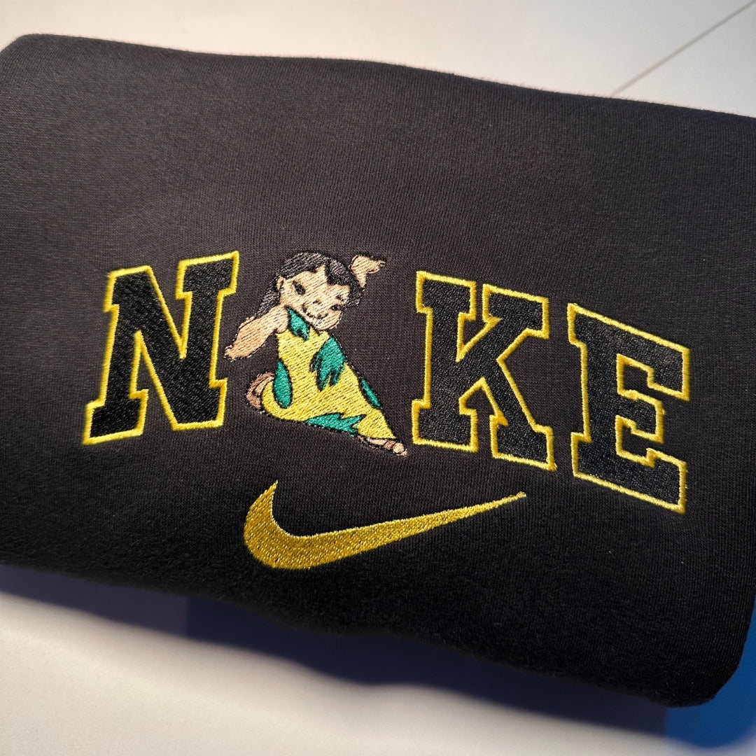 Black fabric with custom embroidered couple shirts design featuring cartoon character integrated into bold yellow and black letters with gold swoosh